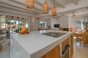 A modern kitchen with a large island, wicker pendant lights, and a view to the outdoors.