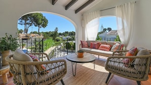 A balcony with wicker furniture, a potted plant, and a view of trees and houses. - Los Jazmines - Javea, Costa Blanca (Javea)