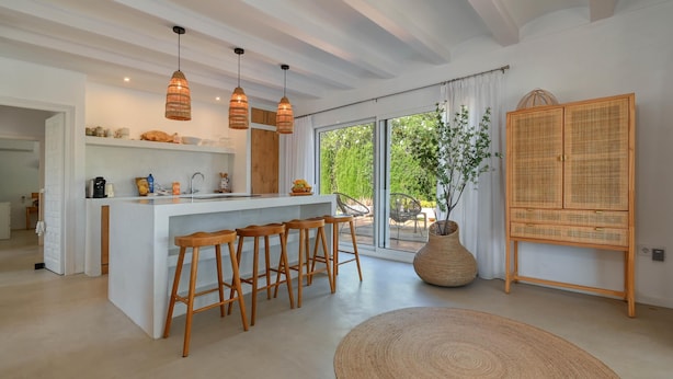 A modern kitchen with a central island, bar stools, pendant lights, and a large window with a view of greenery. - Los Jazmines - Javea, Costa Blanca (Javea)