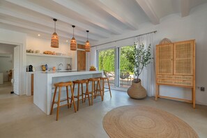 Une cuisine moderne dotée d’un îlot central, de tabourets de bar, de luminaires suspendus et d’une grande fenêtre offrant une vue sur la verdure.
