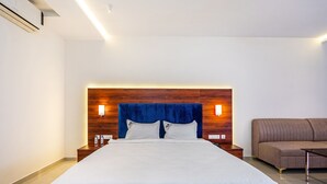 Habitación de hotel con una cama grande, cabecera de madera, lámparas de noche, un sofá marrón y una mesita.