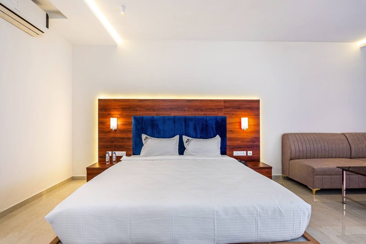 Habitación de hotel con una cama grande, cabecera de madera, lámparas de noche, un sofá marrón y una mesita.
