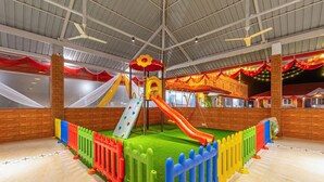 Zona de juegos interior con tobogán, pared de escalada y suelo acolchado.