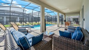 A covered outdoor area with wicker furniture, a pool, and a glass enclosure. - Disney Bliss Themed Rooms, Game Room, Private Pool (Kissimmee)