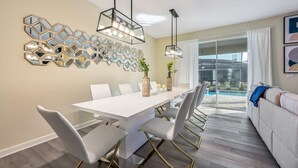 A modern dining area with a white table and chairs, decorative wall mirrors, and pendant lights. - Disney Bliss Themed Rooms, Game Room, Private Pool (Kissimmee)