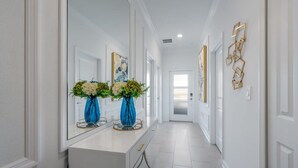 A hallway with a white console table, two blue vases with flowers, and a mirror reflecting the room.
