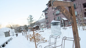 A snow-covered outdoor area with a metal bench and a glass jar on a wooden stand. - ryobou hanaemi (Otaru)