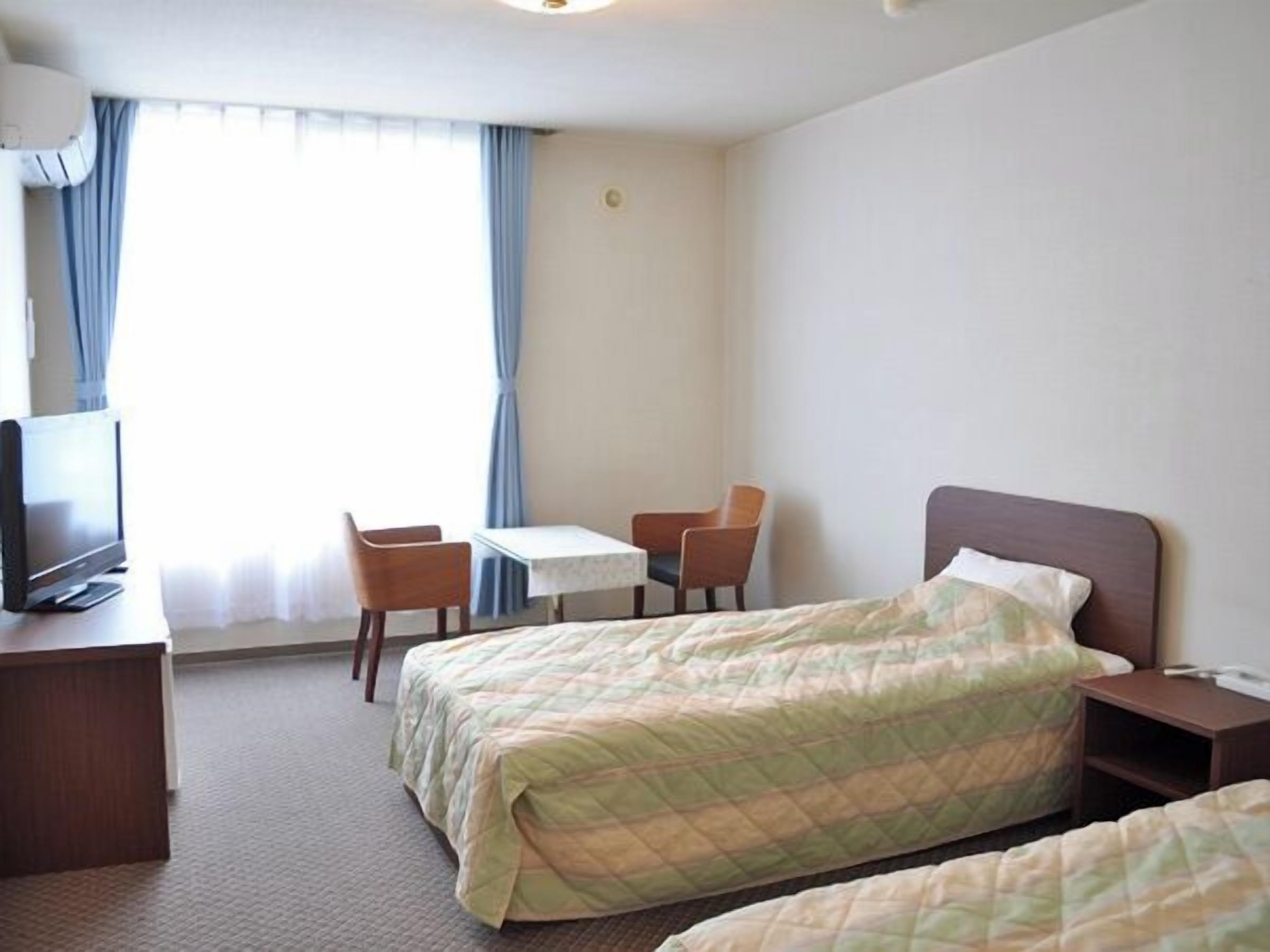 A hotel room with a bed, a desk with a television, two chairs, and a small table.