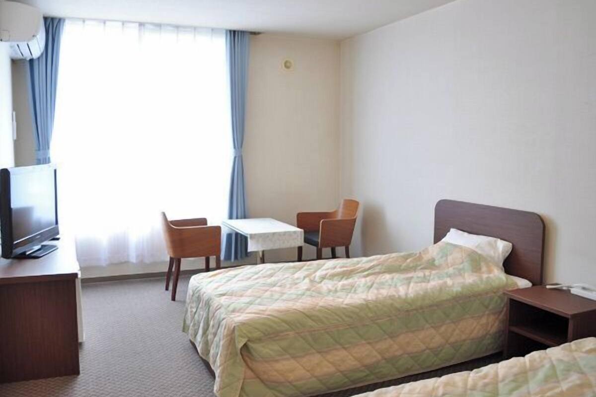 A hotel room with a bed, a desk with a television, two chairs, and a small table.