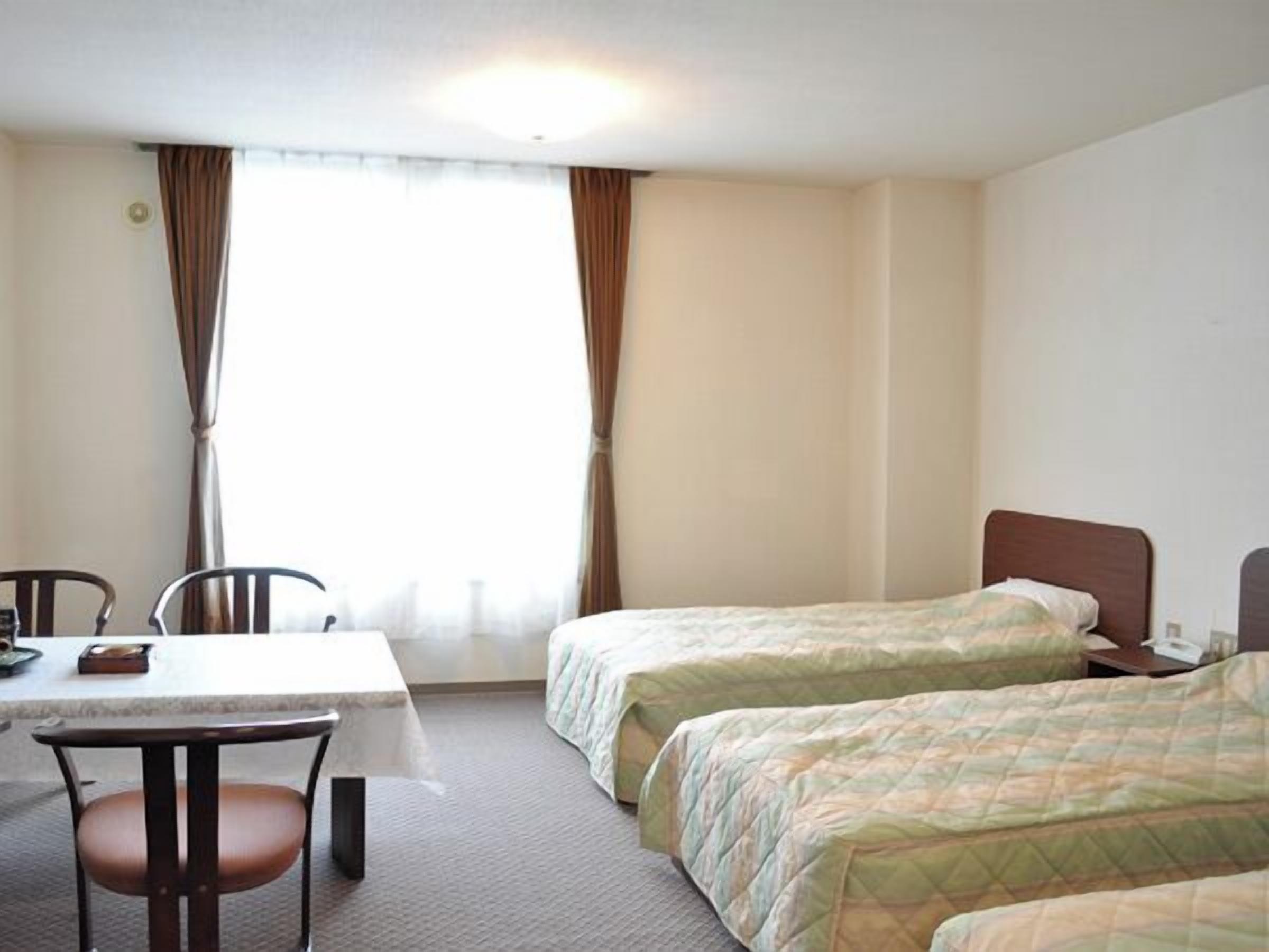A hotel room with two beds, a table, and a chair.