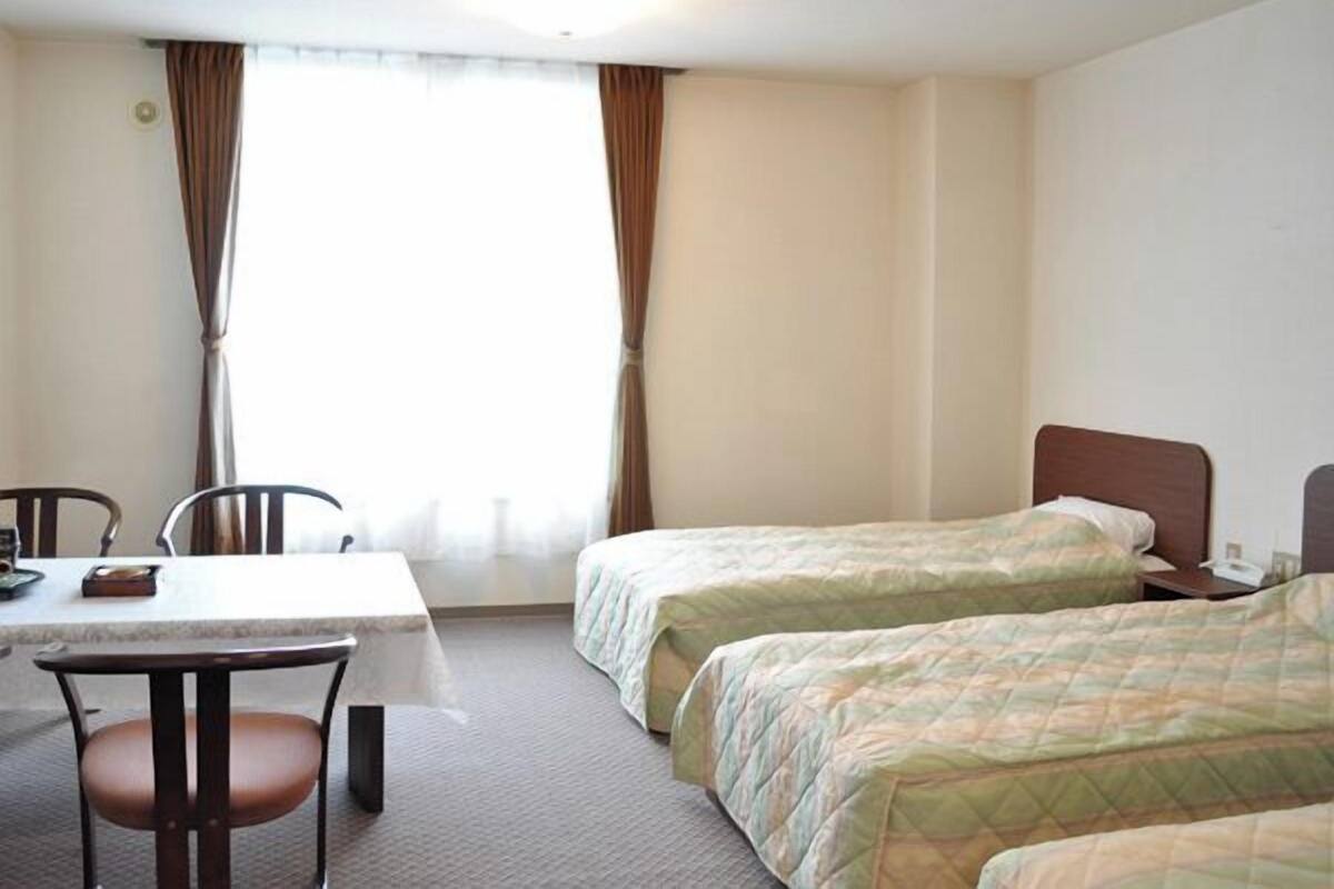 A hotel room with two beds, a table, and a chair.