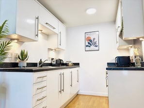 A modern kitchen with white cabinets, a black countertop, a coffee maker, and a framed artwork on the wall.