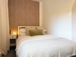 Ein Schlafzimmer mit einem Bett, einem Nachttisch und einer Wand mit vertikalen Hol zleisten.