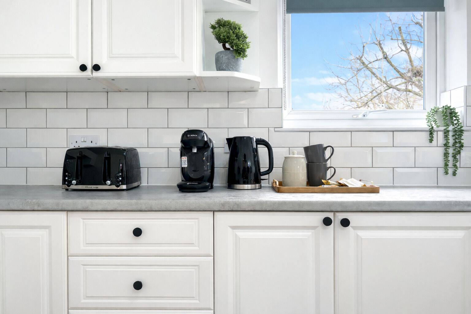 A kitchen with white cabinets, a toaster, a coffee maker, and a tray with cups and a teapot.