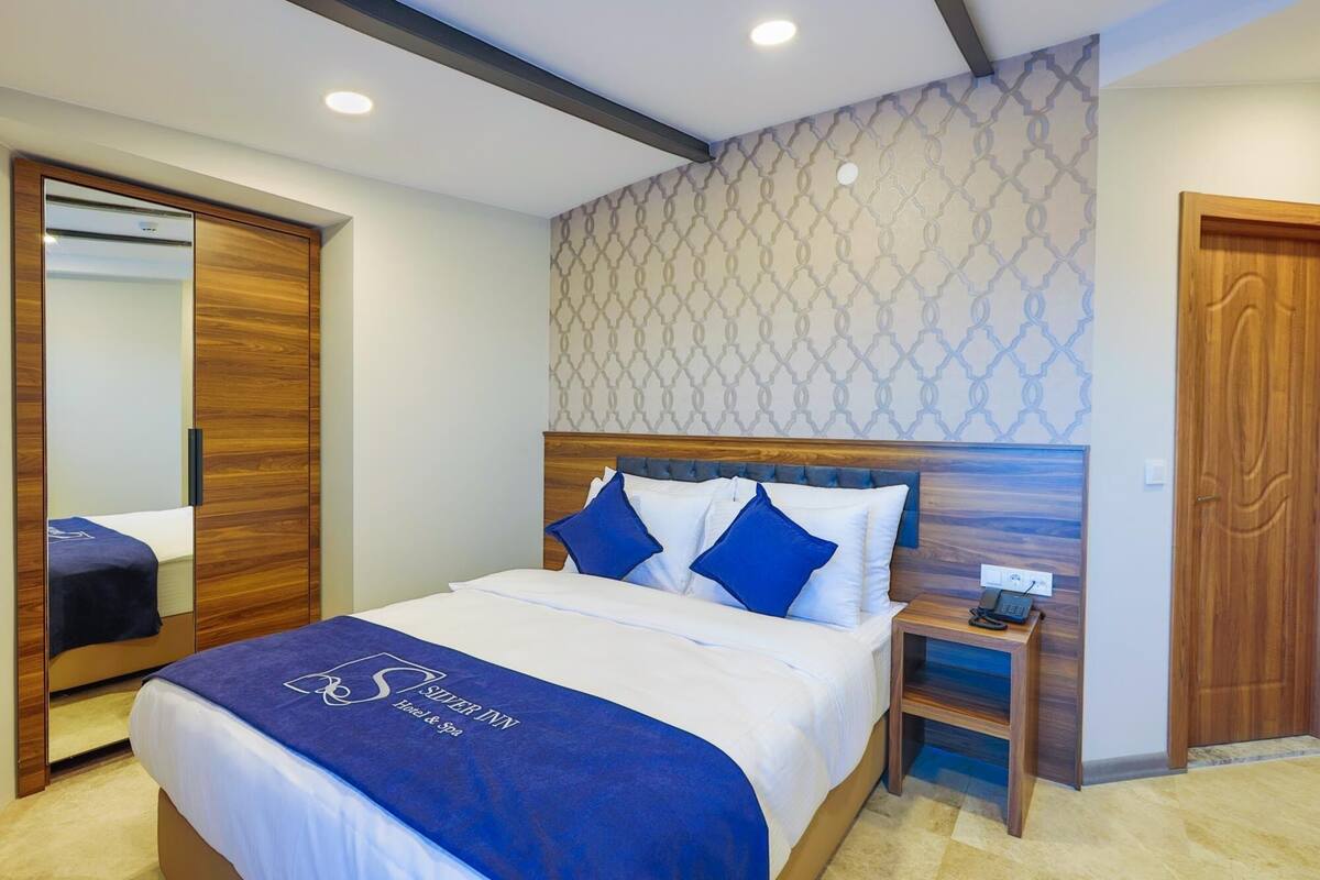 Une chambre d’hôtel avec un lit, une table de chevet, un téléphone et un mur orné d’un motif géométrique.