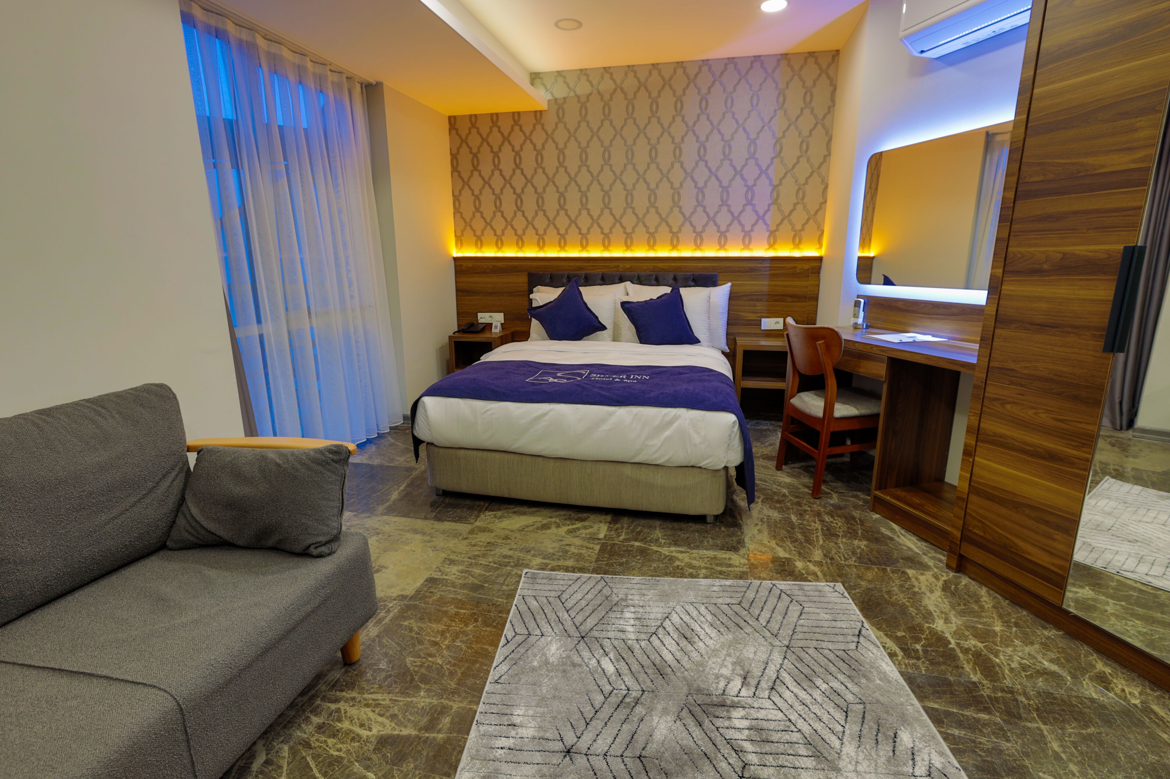 A hotel room with a bed, a desk, a chair, a sofa, and a carpet.