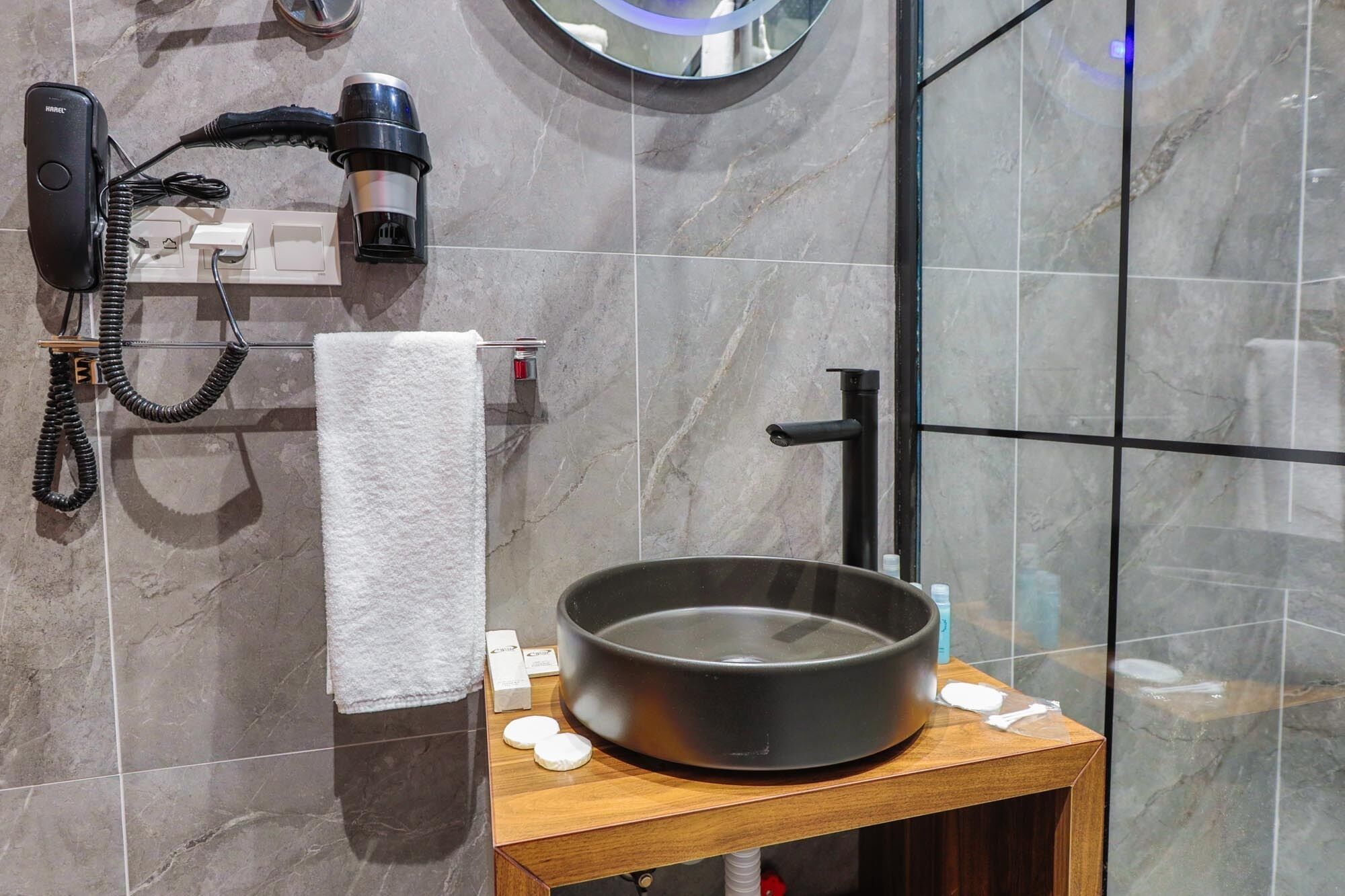 Un bagno con asciugacapelli, asciugamano, lavandino e articoli da toilette su un ripiano in legno.