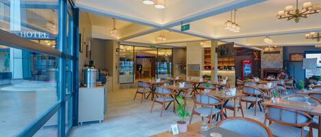 A modern hotel restaurant with wooden tables, chairs, and hanging pendant lights.