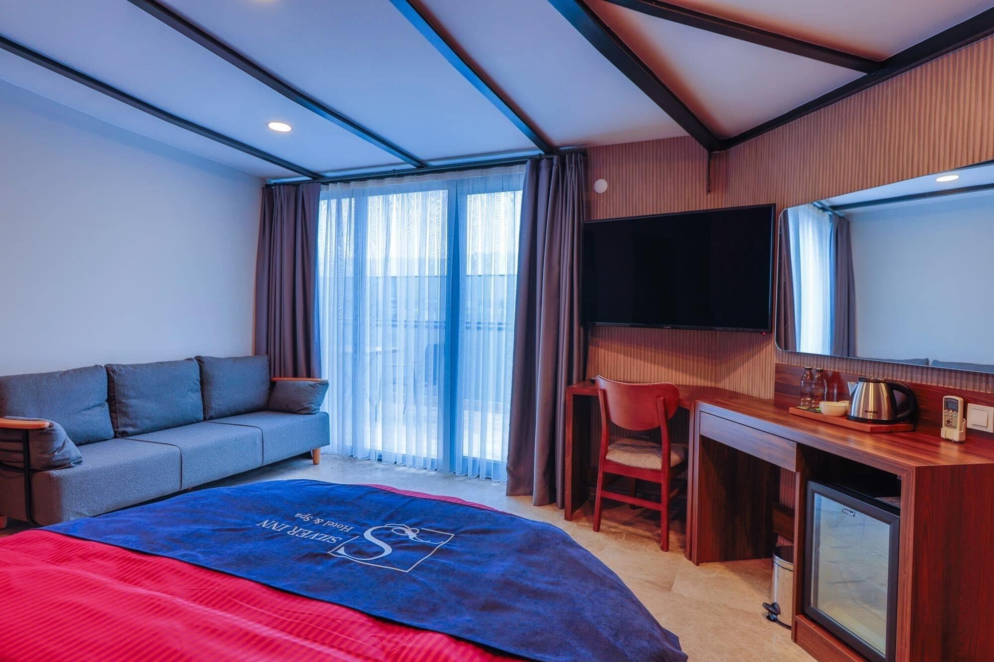 Habitación de hotel con cama, sofá, escritorio, silla, televisor y minibar.