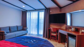 Habitación de hotel con cama, sofá, escritorio, silla, televisor y minibar.