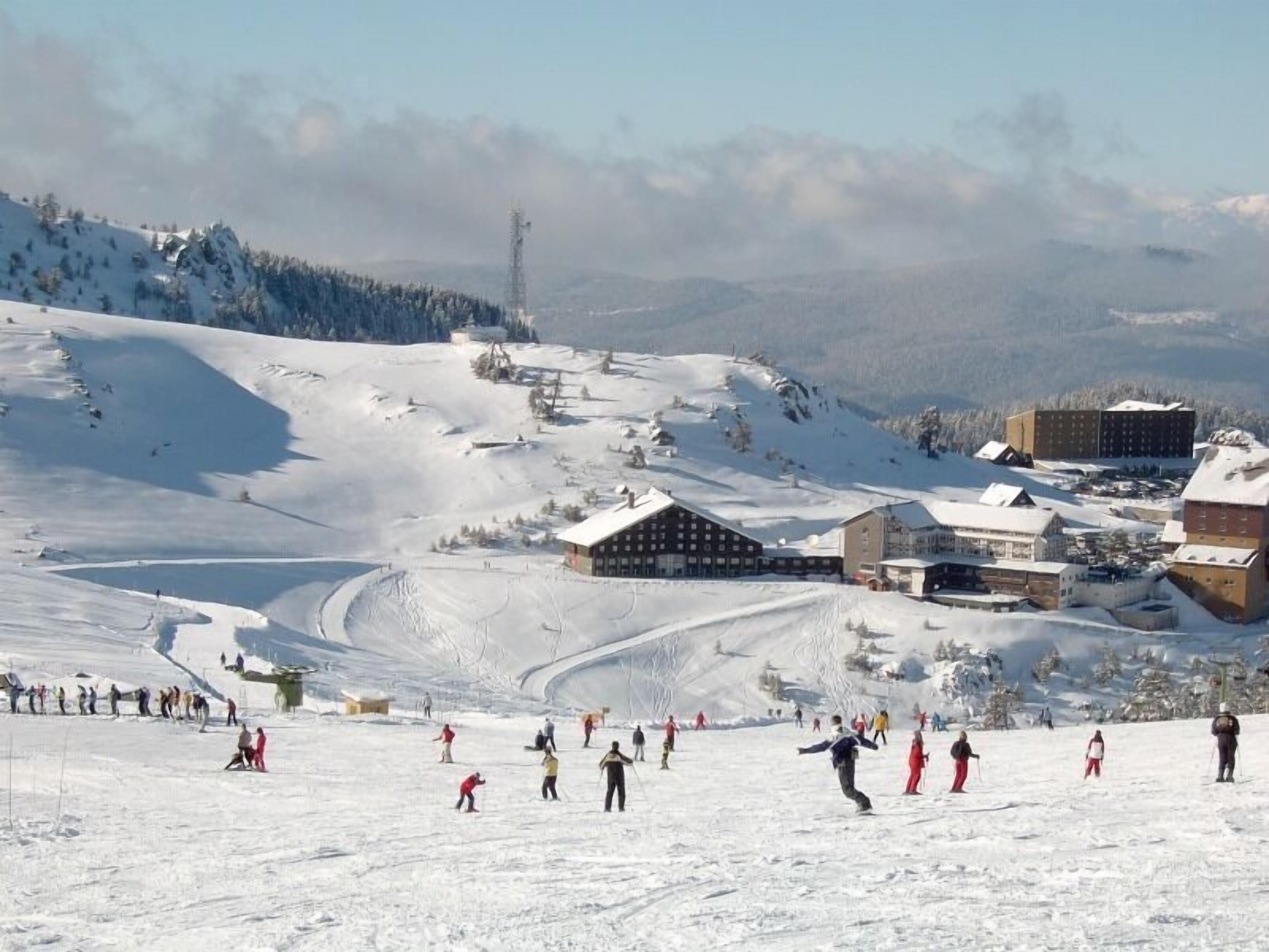 A ski resort with multiple buildings, including a lodge and a ski lift tower, surrounded by snowy slopes and trees.