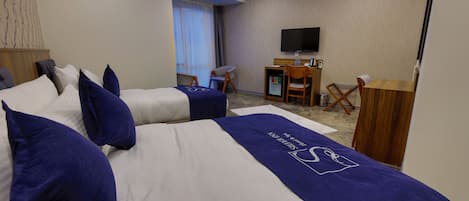A hotel room with two beds, a desk, a chair, a television, and a minibar.