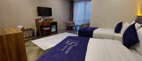 Quarto de hotel com duas camas, uma escrivaninha, uma cadeira, televisão e janela com cortinas.
