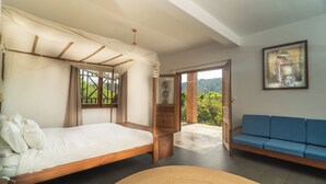 A bedroom with a bed, a blue sofa, and a view of greenery through a window. - Eulophiella (Andasibe)