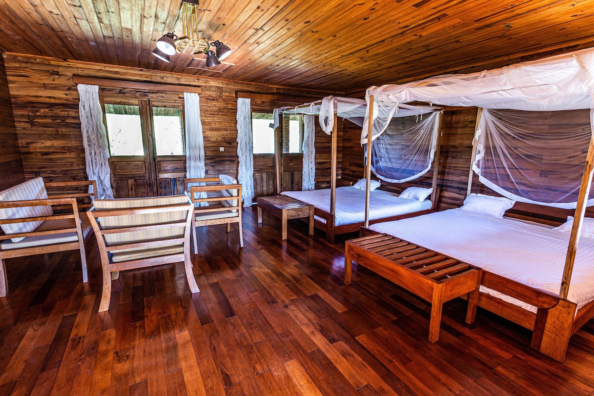 Uma cabana de madeira com quatro camas, cada uma com dossel, e um banco de madeira.