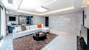 A modern living room with a sectional sofa, a coffee table, and a kitchen in the background. - KOKO Premier Resort (Seogwipo)