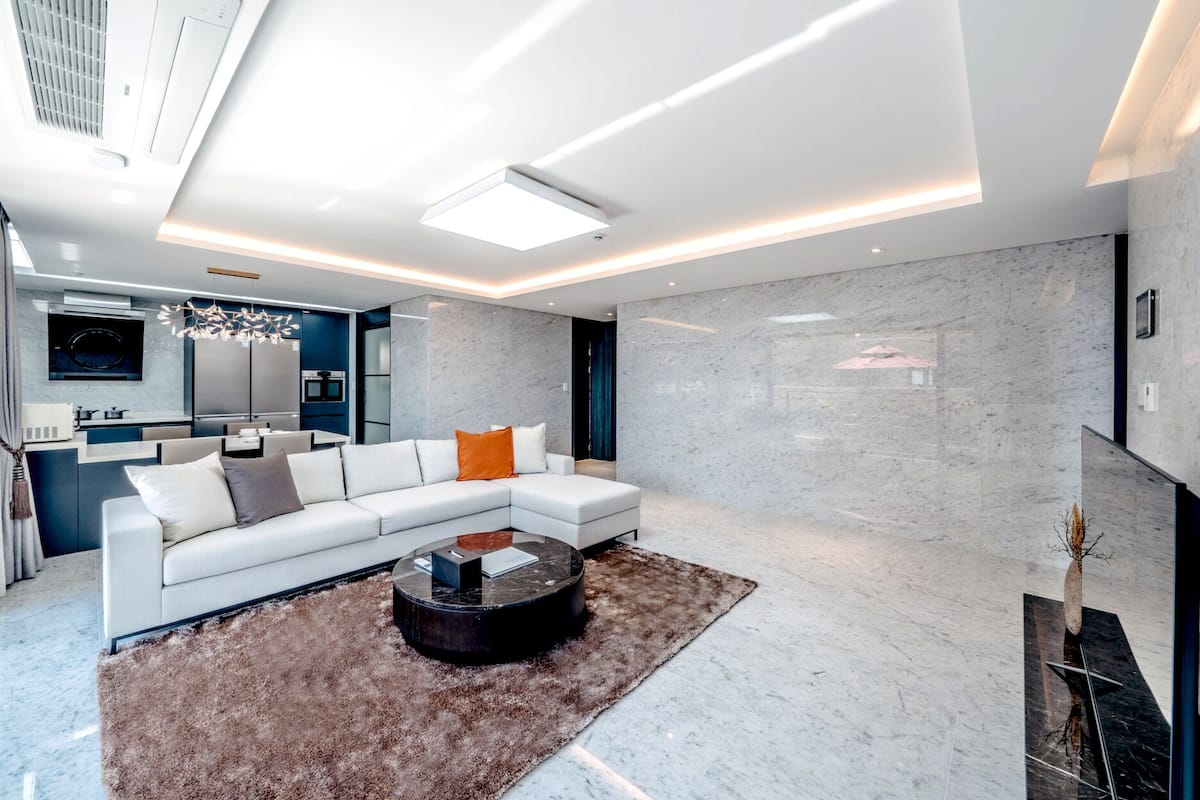 A modern living room with a sectional sofa, a coffee table, and a kitchen in the background.