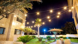 An outdoor patio area with string lights, palm trees, and outdoor furniture. - KOKO Premier Resort (Seogwipo)
