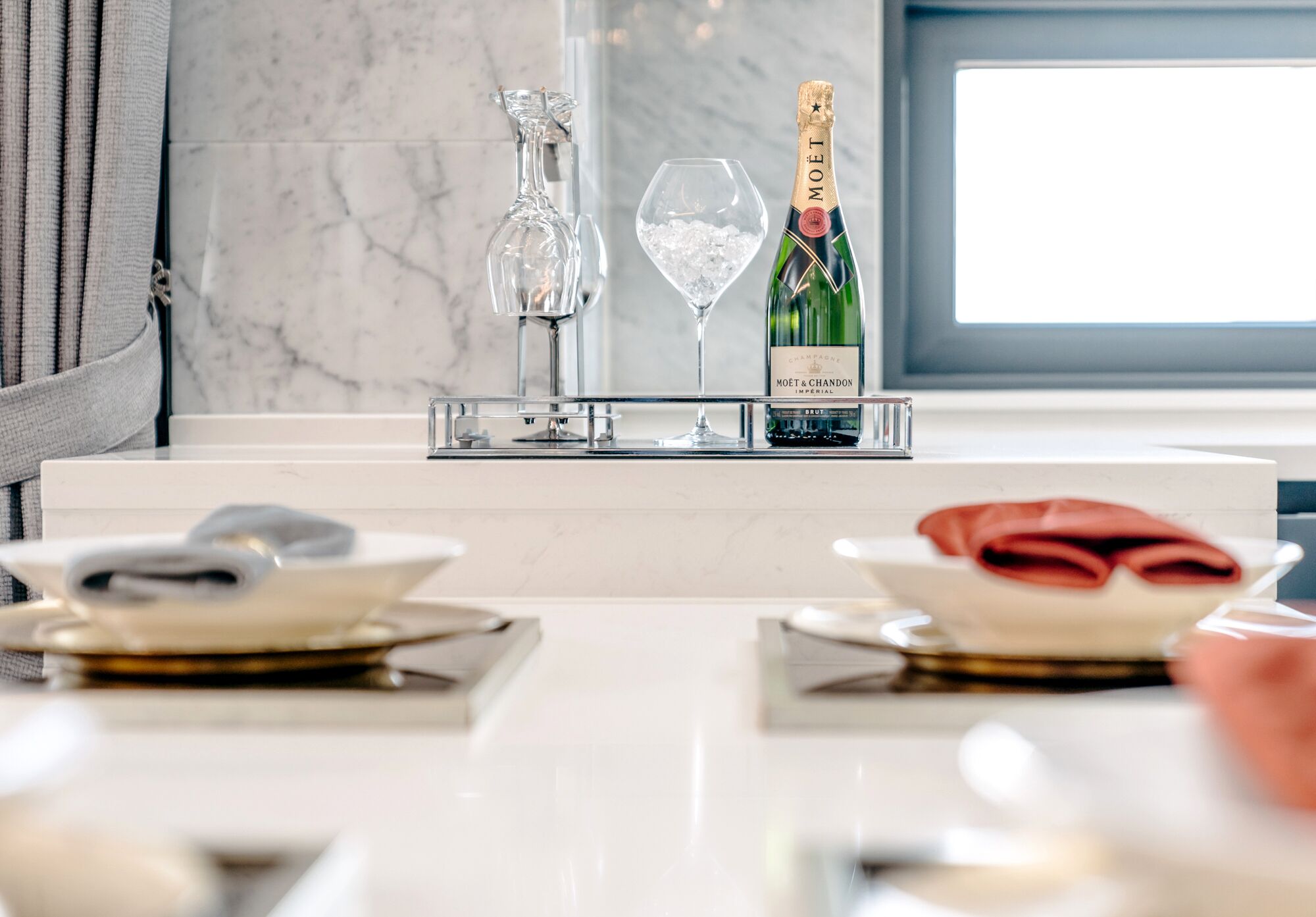 Uma mesa de jantar posta com pratos, um copo de água, uma garrafa de champanhe Moët & Chandon e um jarro para vinho.