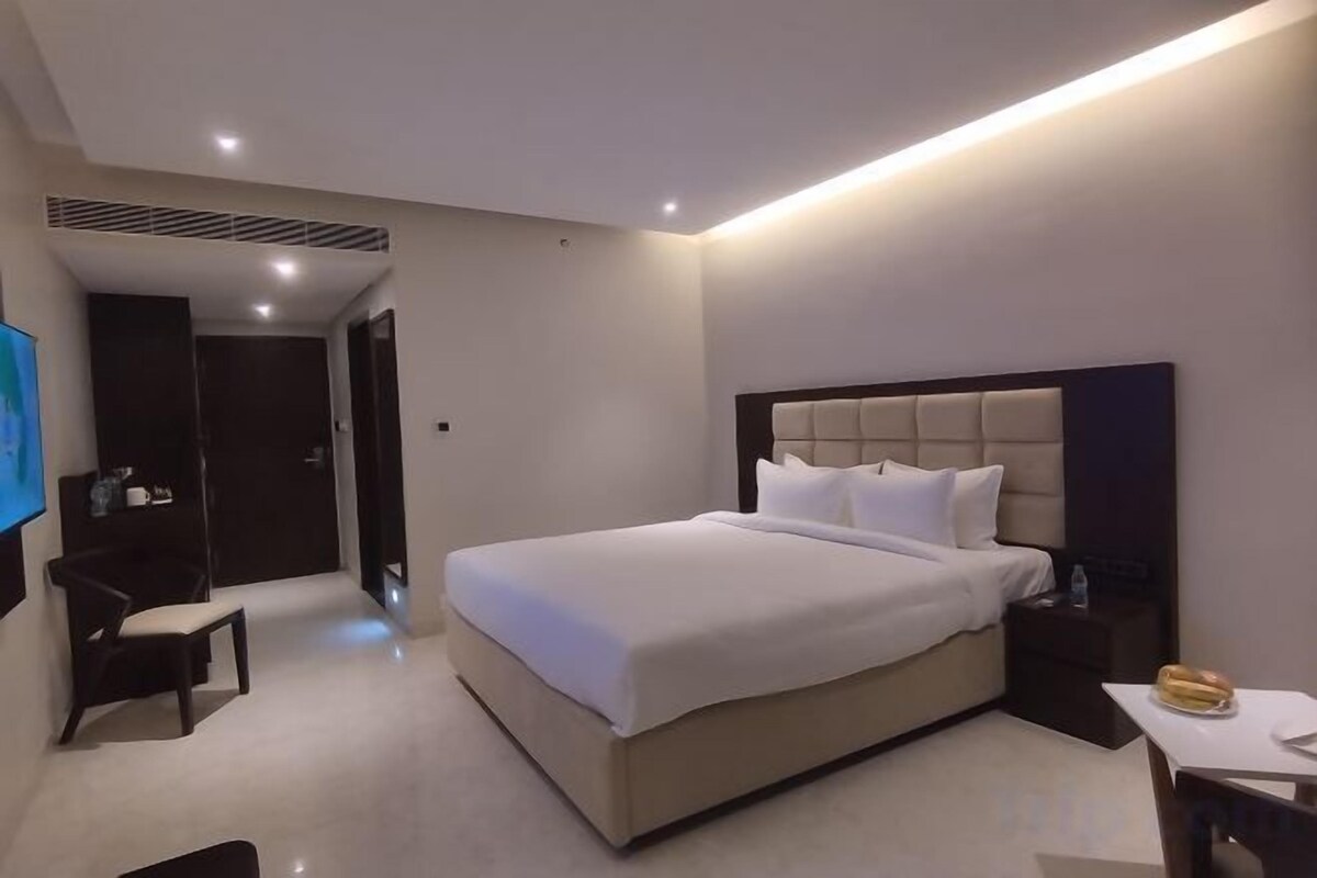 A modern hotel room with a large bed, bedside tables, a desk, and a TV.