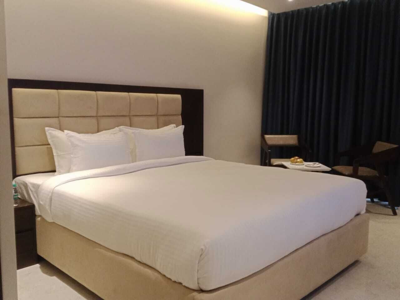 A hotel room with a large bed, a nightstand, a chair, and a dark curtain.