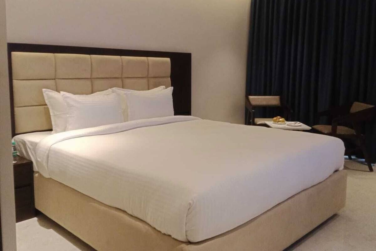 Une chambre d’hôtel avec un grand lit, une table de chevet, une chaise et un rideau foncé.