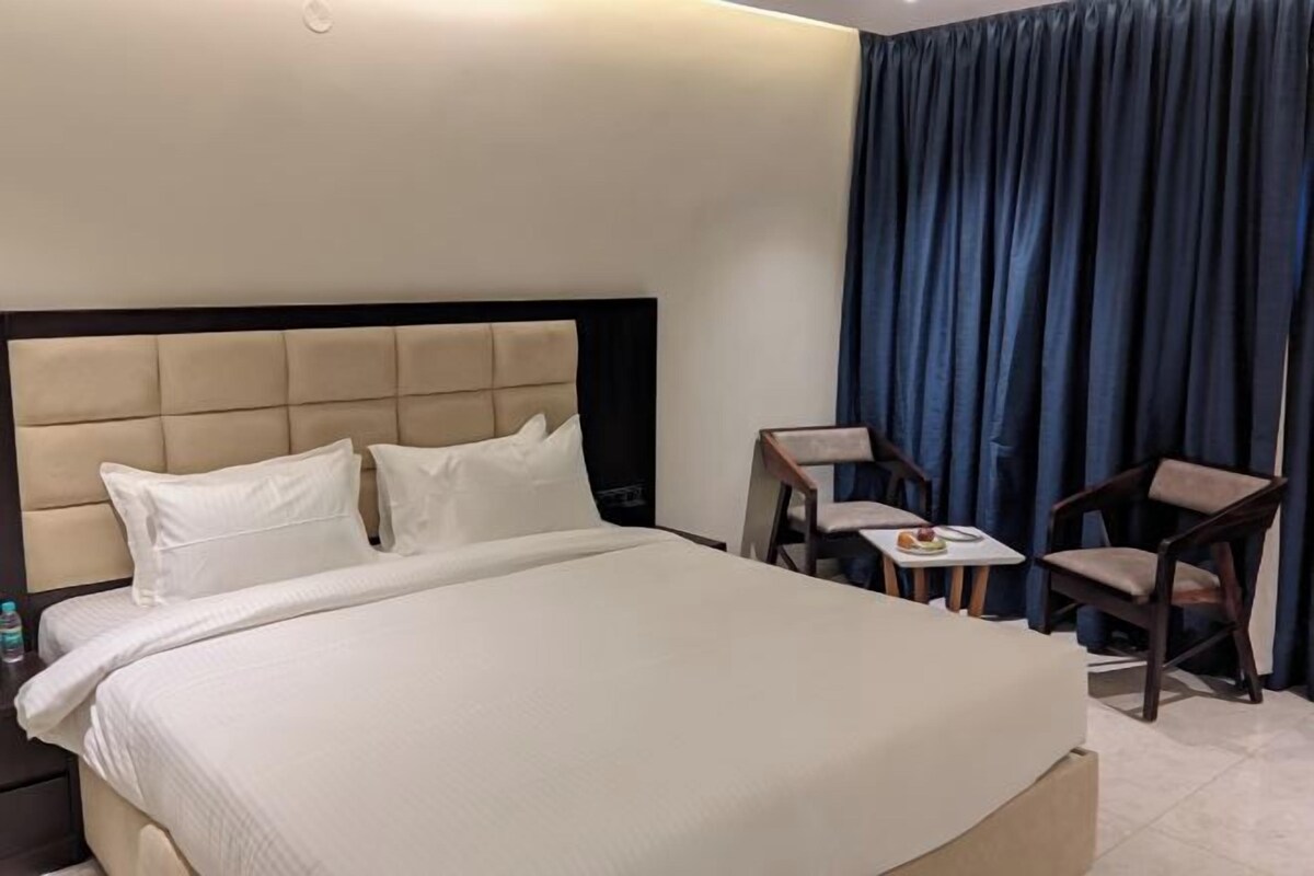 Habitación de hotel con una cama grande, una mesa pequeña con sillas y vistas al exterior a través de una ventana con cortinas azules.