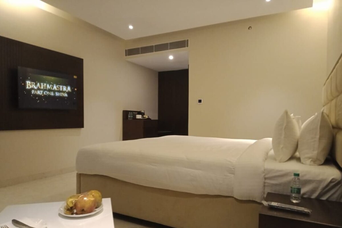 A hotel room with a bed, a TV on the wall, a small table with a plate of food, and a water bottle on the side table.