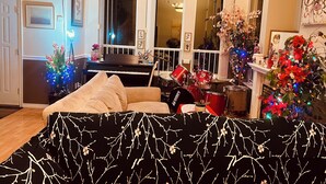 A living room with a piano, a drum set, a sofa, and a Christmas tree.