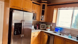 A kitchen with wooden cabinets, stainless steel appliances, a microwave, a toaster, a dishwasher, and a window with a view.