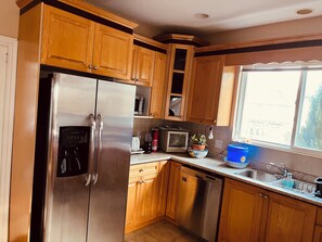A kitchen with wooden cabinets, stainless steel appliances, a microwave, a toaster, a dishwasher, and a window with a view.