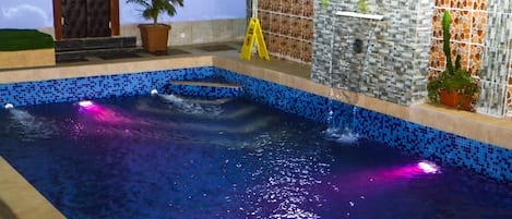 Une piscine bordée de mosaïques bleues, avec un escalier et des plantes en pot.