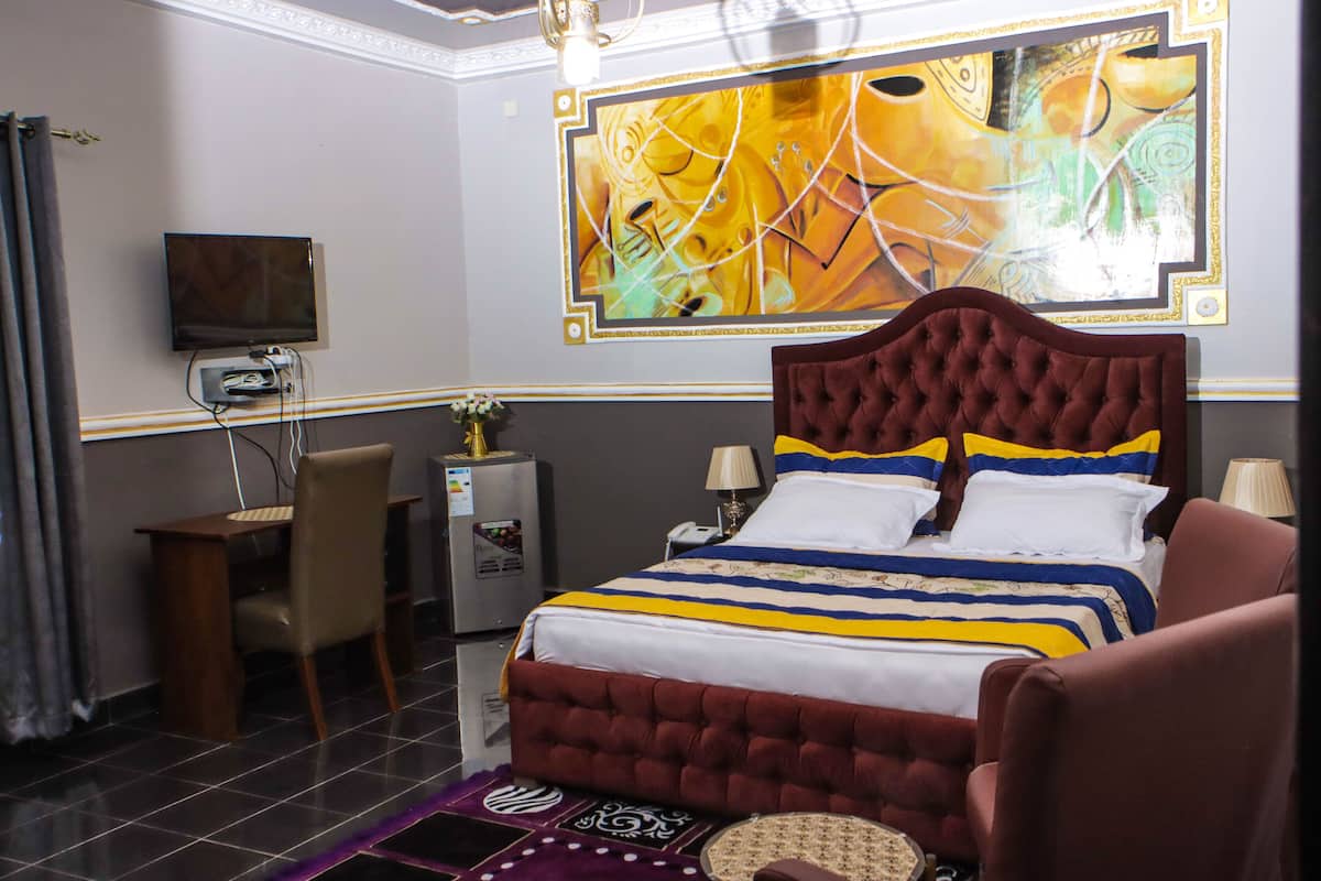 Habitación de hotel con cama, escritorio, silla, televisor y un cuadro abstracto grande en la pared.
