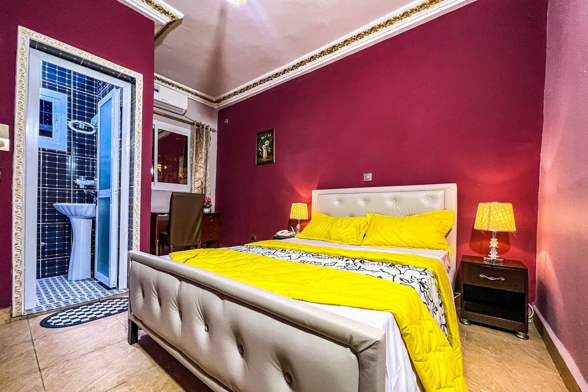 Un dormitorio con cama, mesitas de noche, un espejo, un lavabo y una puerta que da al baño.