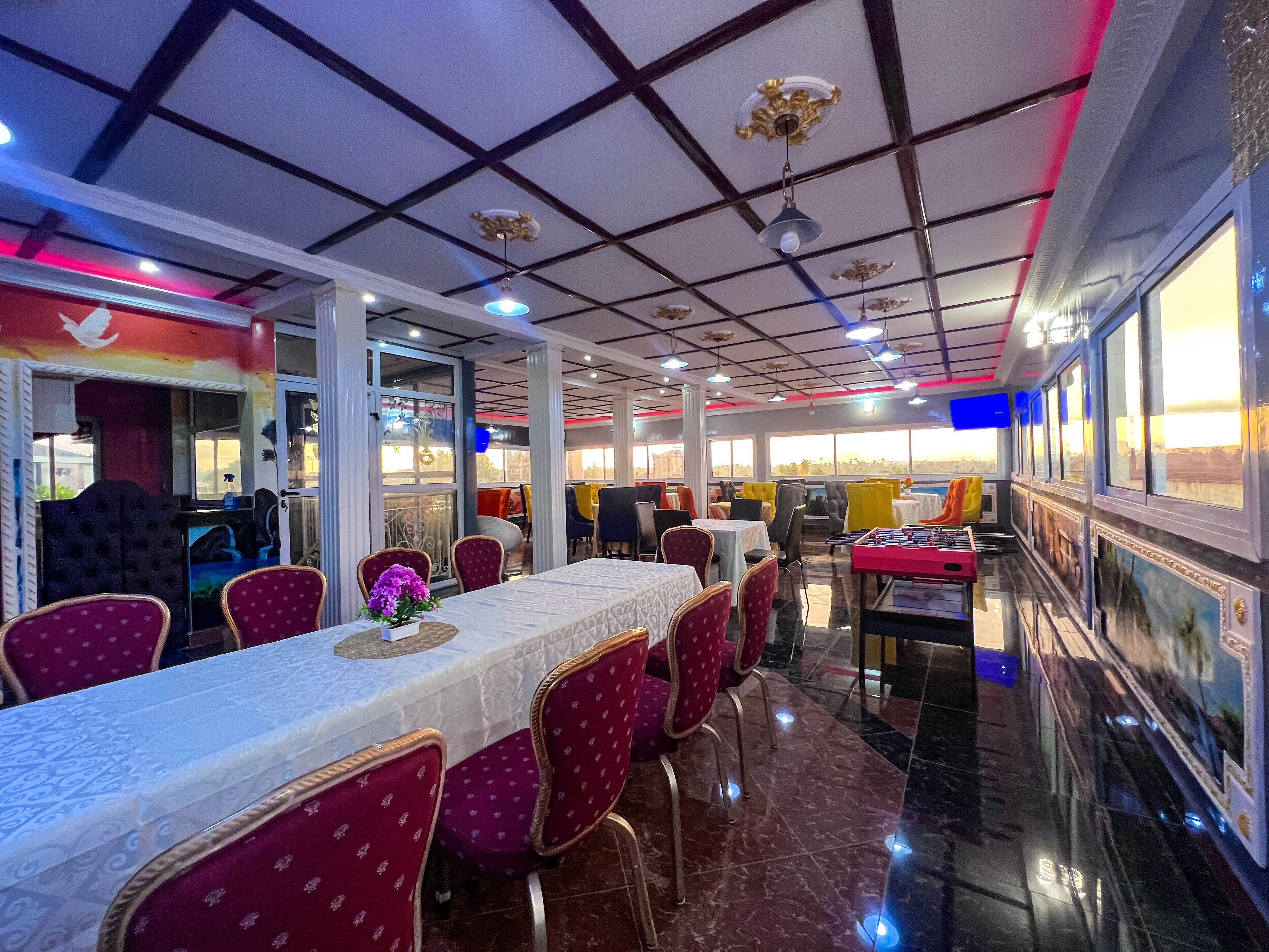 Un restaurante con una larga mesa de comedor, sillas tapizadas de rojo y vistas de la ciudad a través de amplias ventanas.