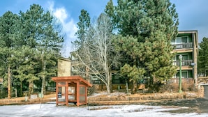 A building with a green exterior and a wooden structure in front. - Angel Fire Condo Mountain Retreat by Velo (Angel Fire)