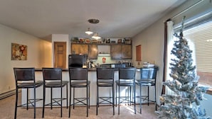 A kitchen with a bar area, a refrigerator, and a Christmas tree by the window. - Angel Fire Condo Mountain Retreat by Velo (Angel Fire)