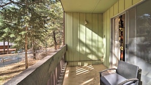 A balcony with a chair and a table, overlooking a street and trees. - Angel Fire Condo Mountain Retreat by Velo (Angel Fire)