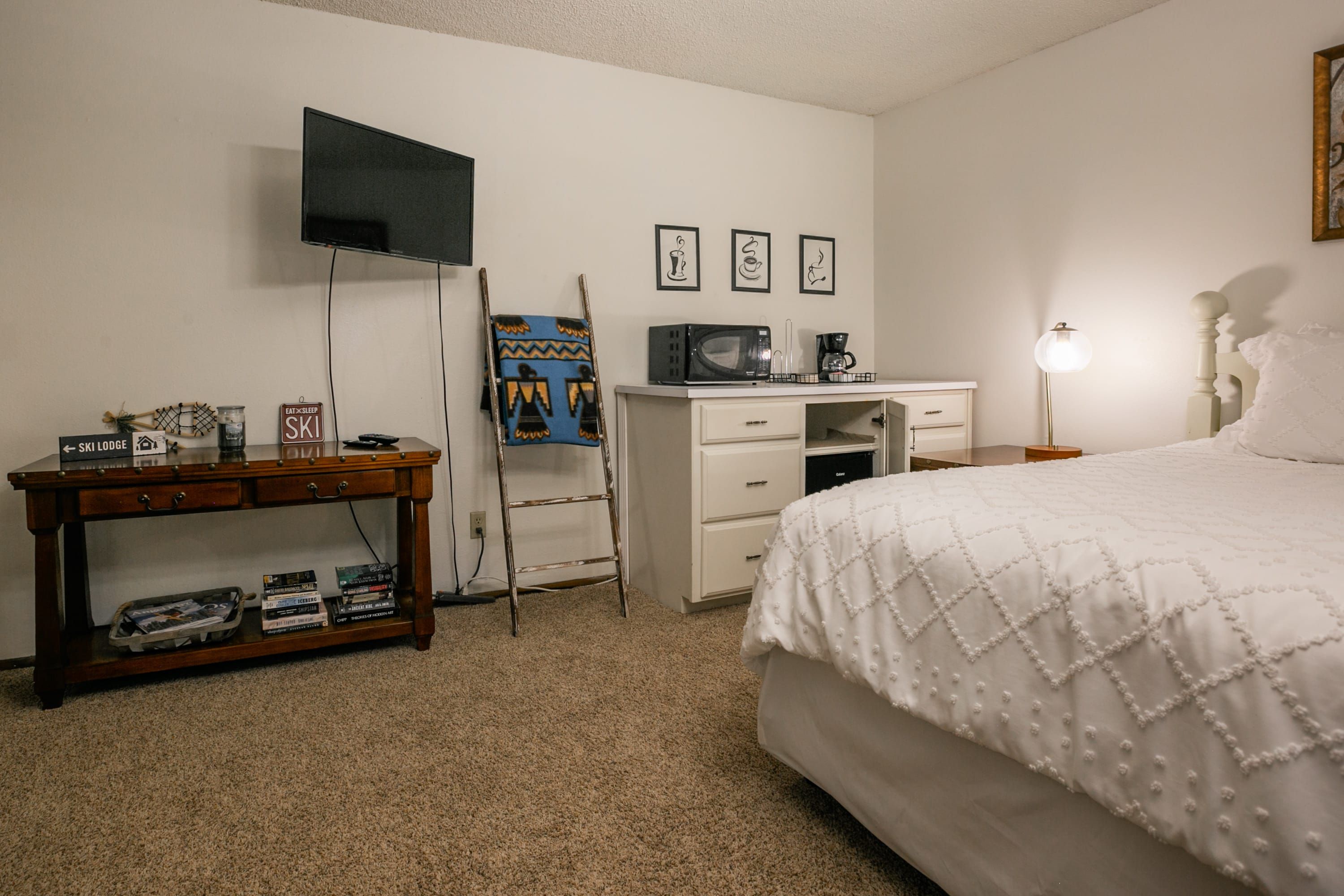 Quarto com cama, escrivaninha, televisão, cafeteira e abajur.