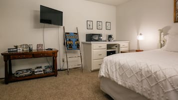 Quarto com cama, escrivaninha, televisão, cafeteira e abajur.